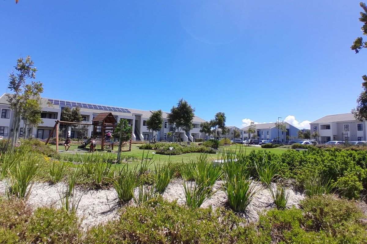 A well-maintained communal garden area featuring landscaped greenery, a children's play structure, and apartment buildings with roof-mounted solar panels.