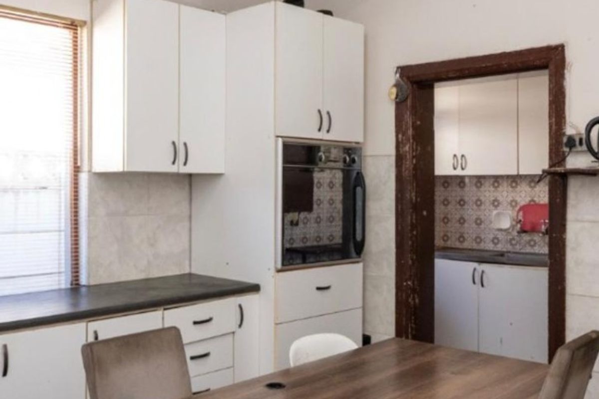 A dated kitchen featuring built-in cabinetry, an integrated oven, and a separate scullery area with tiled backsplash and worn wooden door frames.