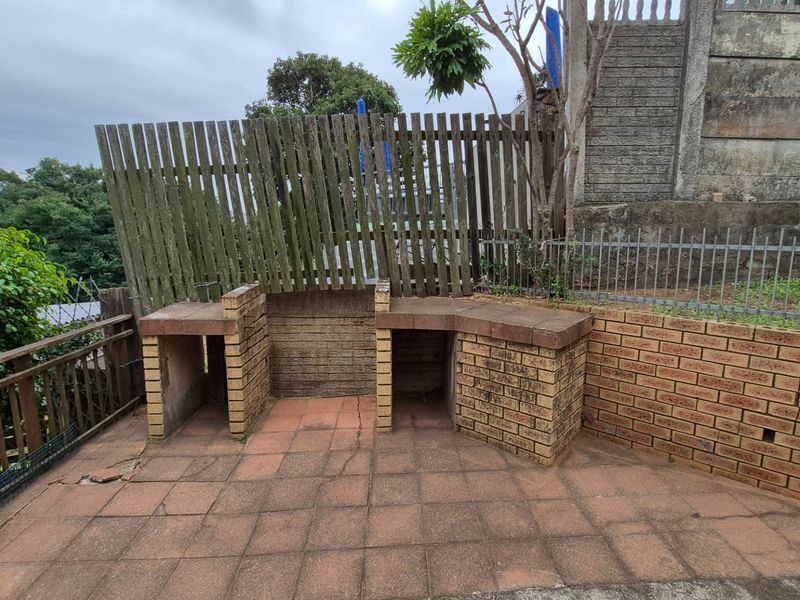 Outdoor patio area featuring a built-in brick braai, paved flooring, and perimeter fencing, offering a functional space for outdoor cooking and entertainment.