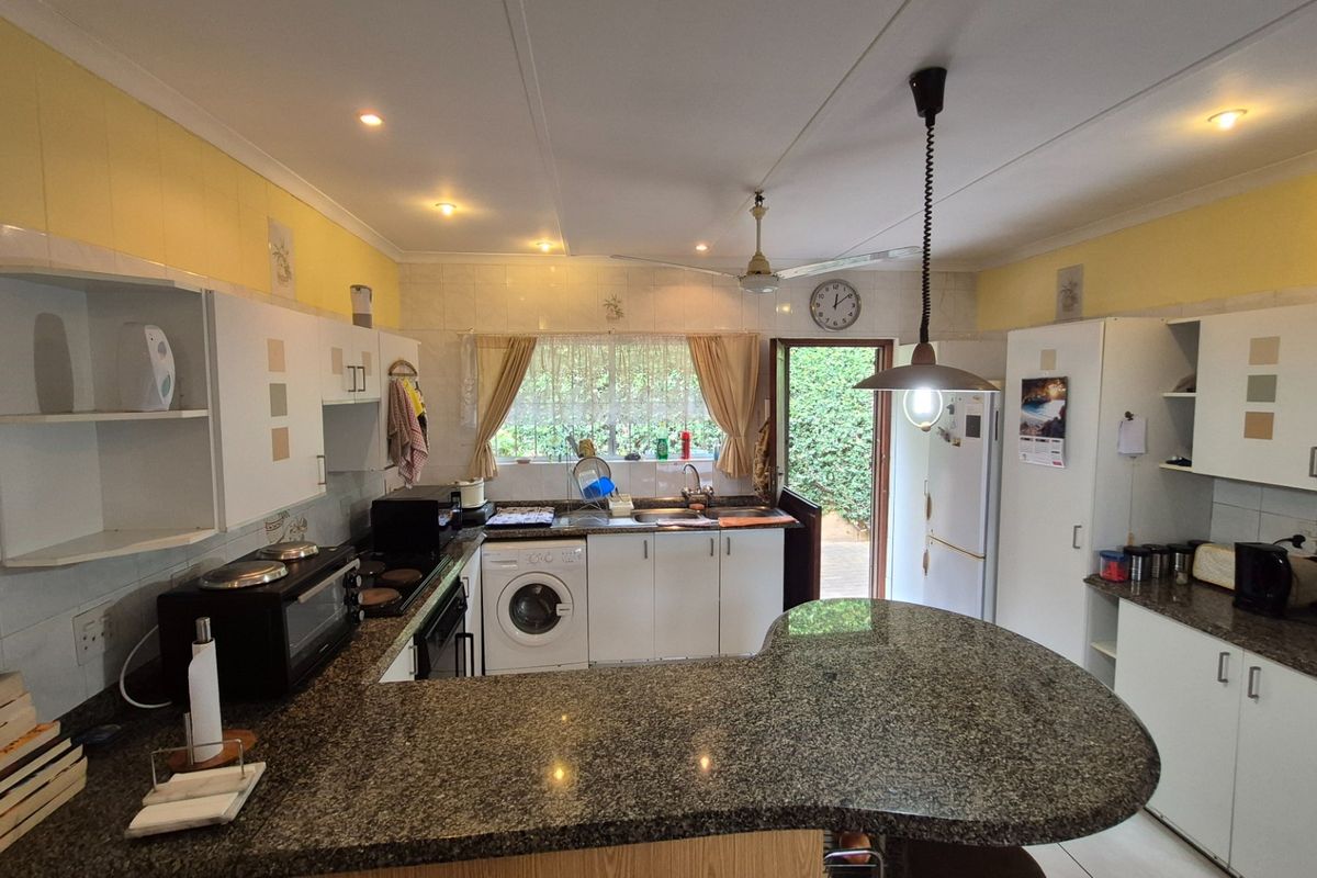 A functional kitchen featuring granite countertops, ample built-in cabinetry, integrated sink, and built-in cooking appliances with direct access to the rear garden.