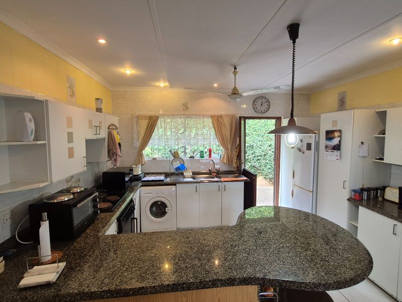 A functional kitchen featuring granite countertops, ample built-in cabinetry, integrated sink, and built-in cooking appliances with direct access to the rear garden.