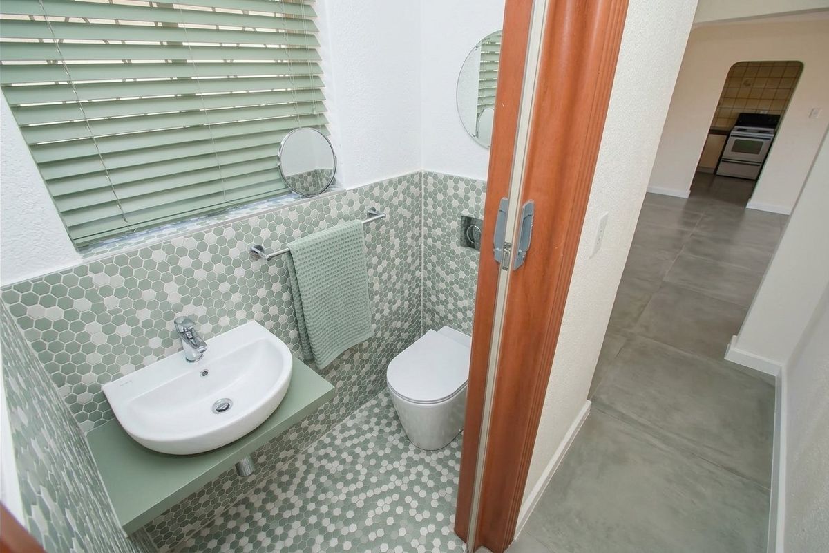 A modern guest bathroom featuring a wall-mounted basin, wall-hung toilet, and stylish green mosaic tiling throughout the floor and walls.