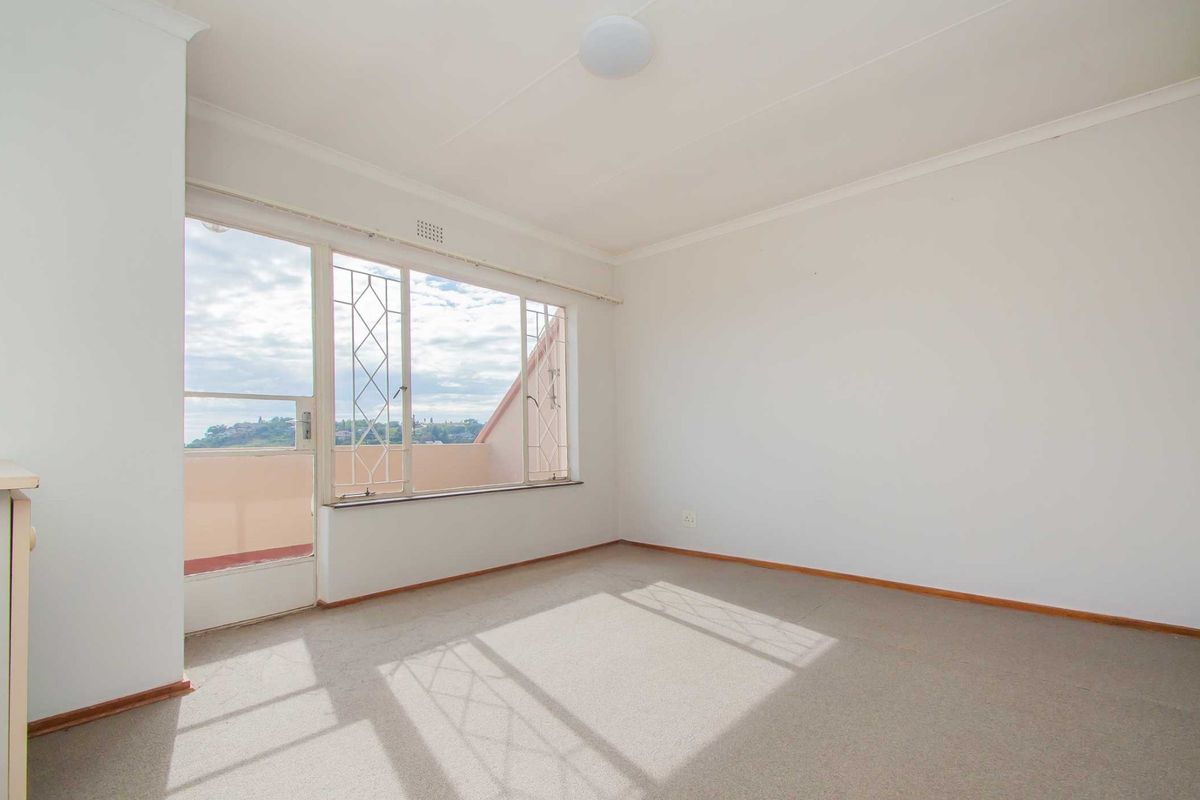 A bright, empty bedroom featuring carpeted flooring, coving, and a sliding door providing access to a balcony with scenic views.