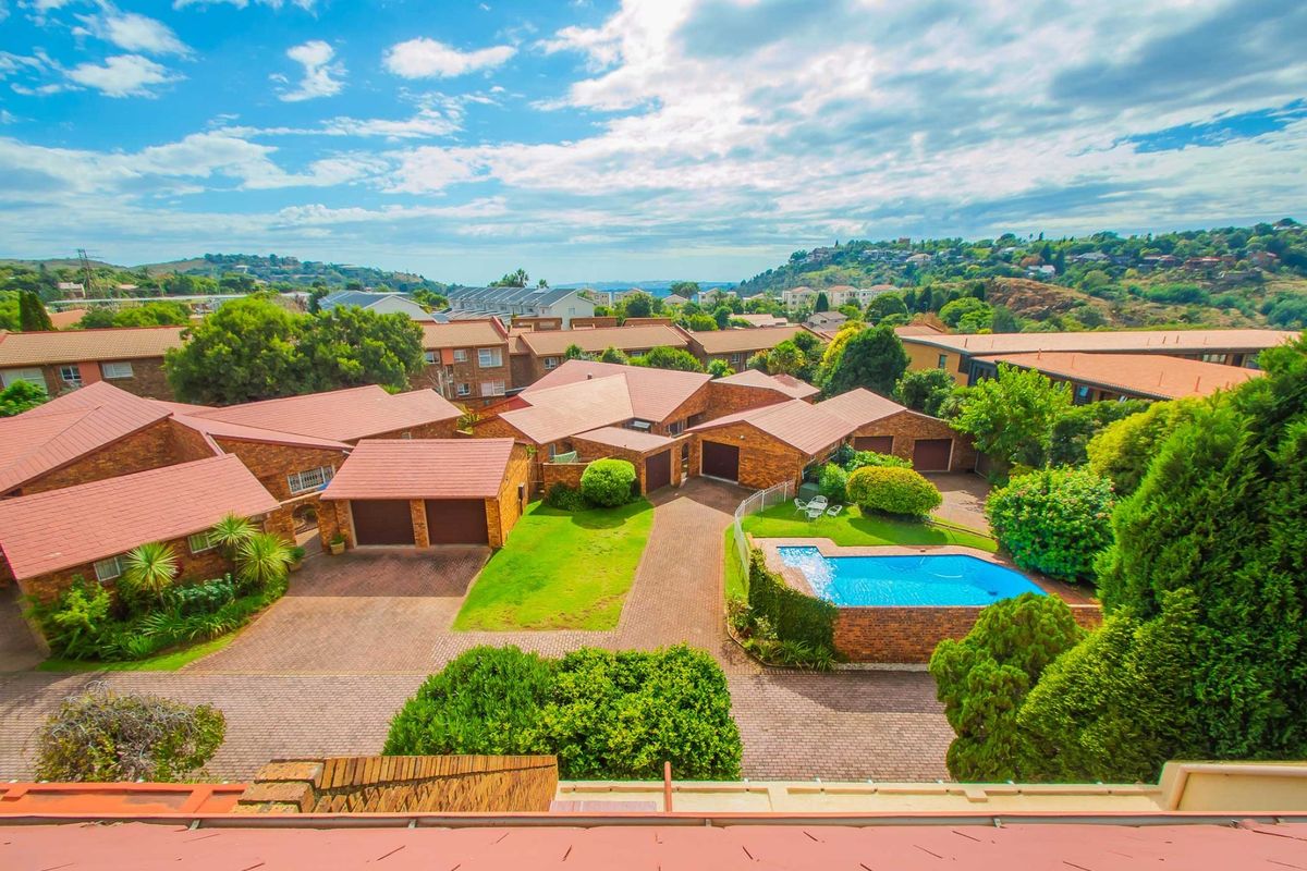 Aerial view of a residential complex featuring multiple brick units with tiled roofs, paved driveways, and a communal swimming pool area.