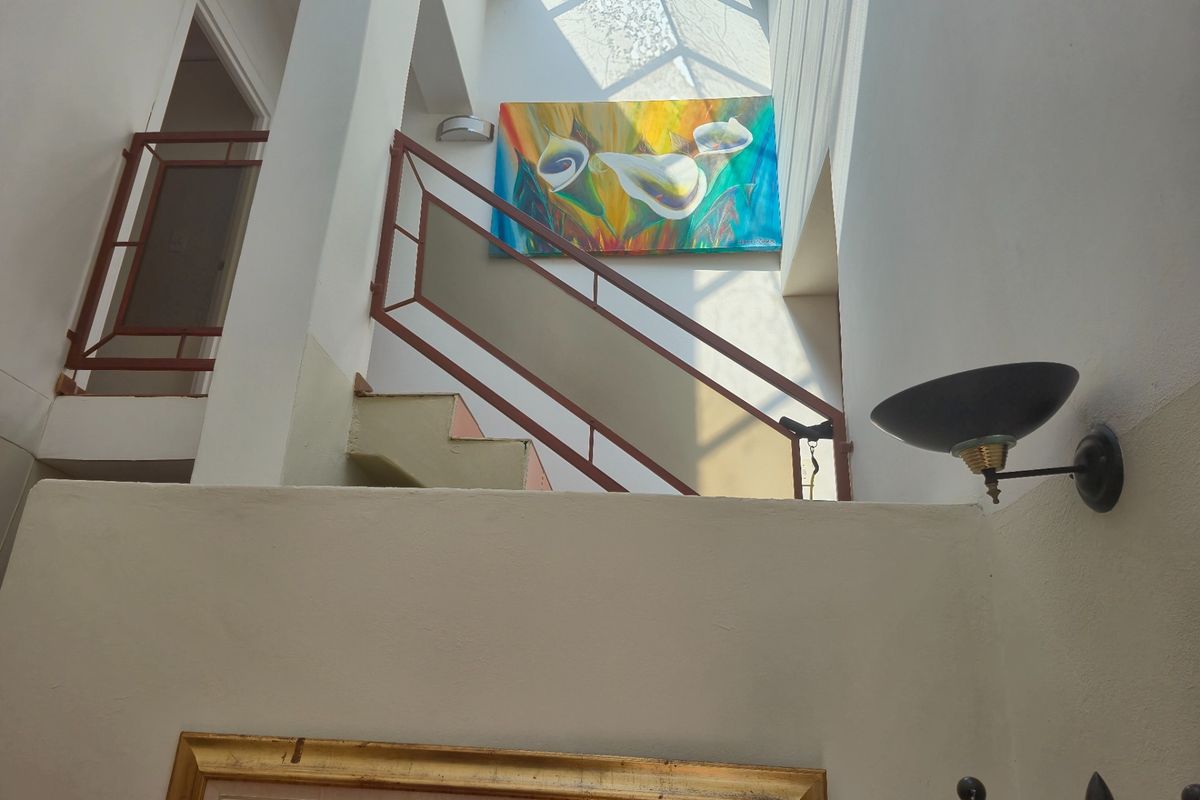 A bright hallway featuring a staircase with metal handrails and a large overhead skylight, creating an airy and well-lit transition space.