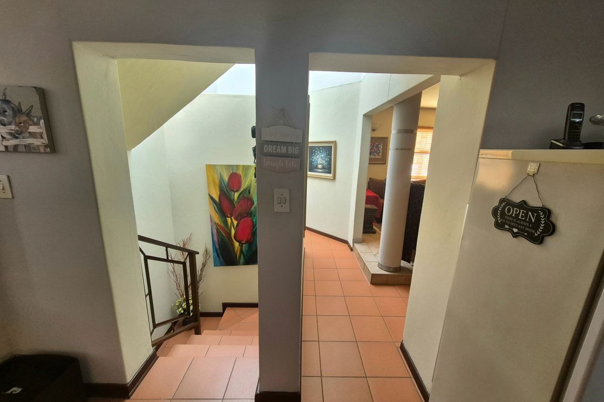 A tiled hallway featuring a staircase with a metal handrail and a structural column, providing access to adjacent living areas.