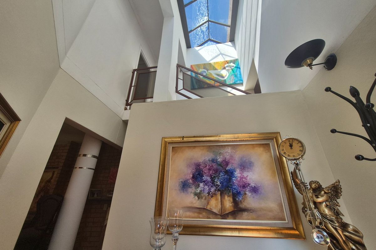 Spacious double-volume entrance hall featuring a large overhead skylight, mezzanine landing, and architectural column detail, creating a bright and airy atmosphere.