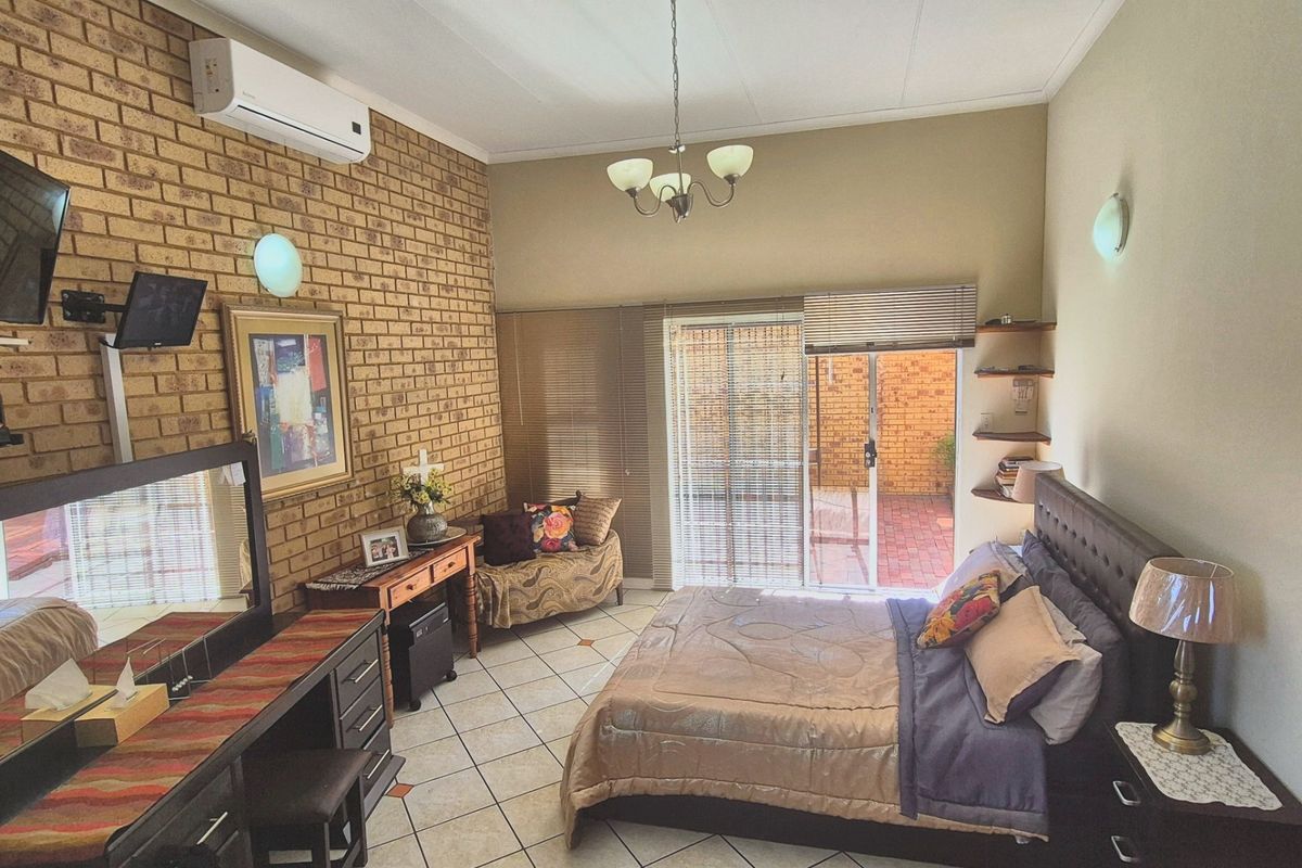 Spacious bedroom featuring an exposed brick feature wall, tiled flooring, and direct access to an outdoor patio area through sliding glass doors.