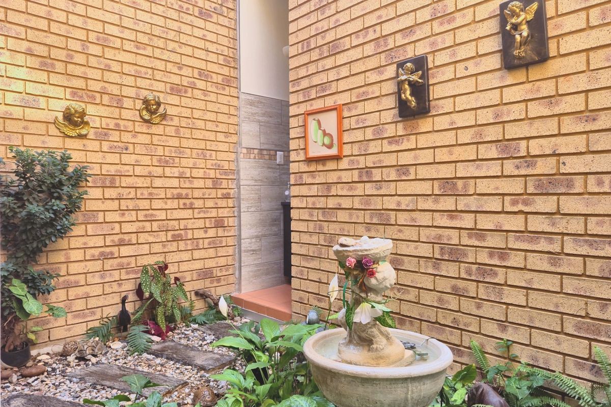 A private courtyard area featuring exposed brick walls, a stone fountain, and landscaped garden beds with stone pathway pavers.