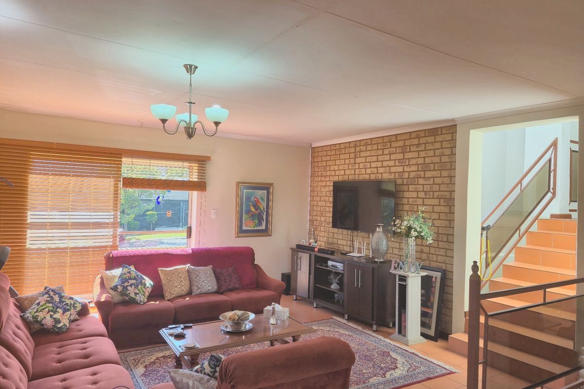Spacious living room featuring an exposed brick wall, tiled flooring, and an integrated staircase with metal railings, offering a warm and functional family space.