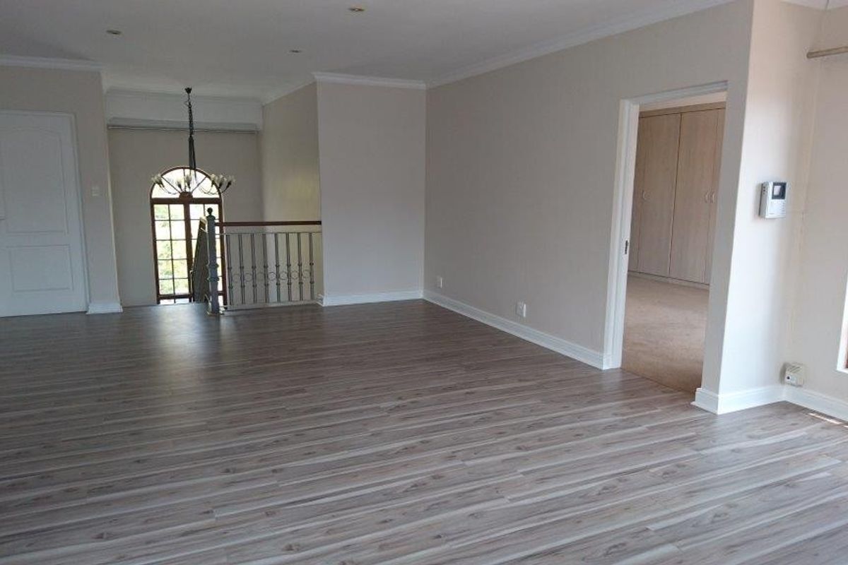 Spacious, light-filled living area featuring modern laminate flooring, recessed lighting, and an elegant arched window overlooking the staircase.