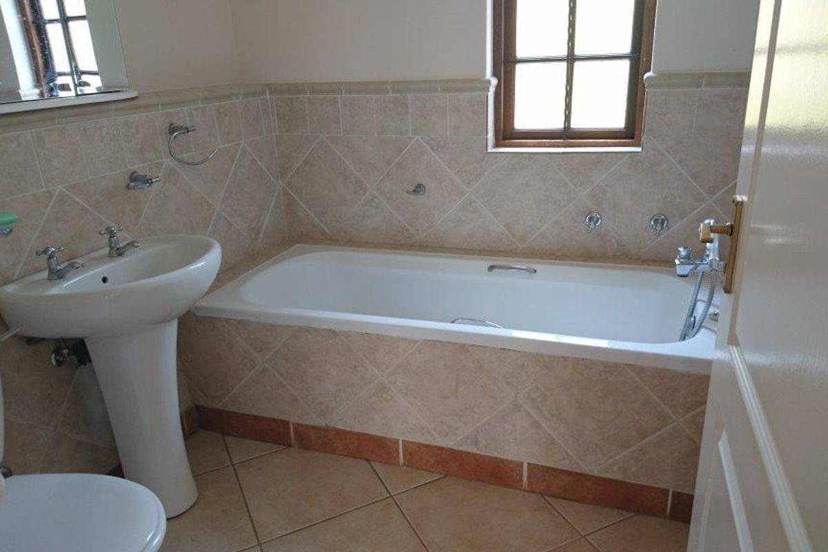 A functional bathroom featuring a built-in bathtub, pedestal basin, and neutral ceramic tiling throughout.