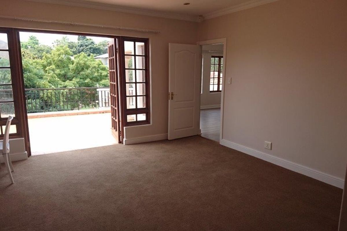 Spacious bedroom featuring built-in cupboards, carpeted flooring, and direct access to a private balcony through classic french doors.