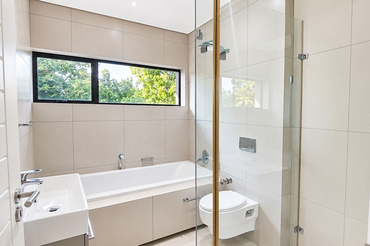 Modern bathroom featuring a built-in bathtub, wall-mounted toilet, glass shower enclosure, and contemporary tiled finishes with ample natural light.