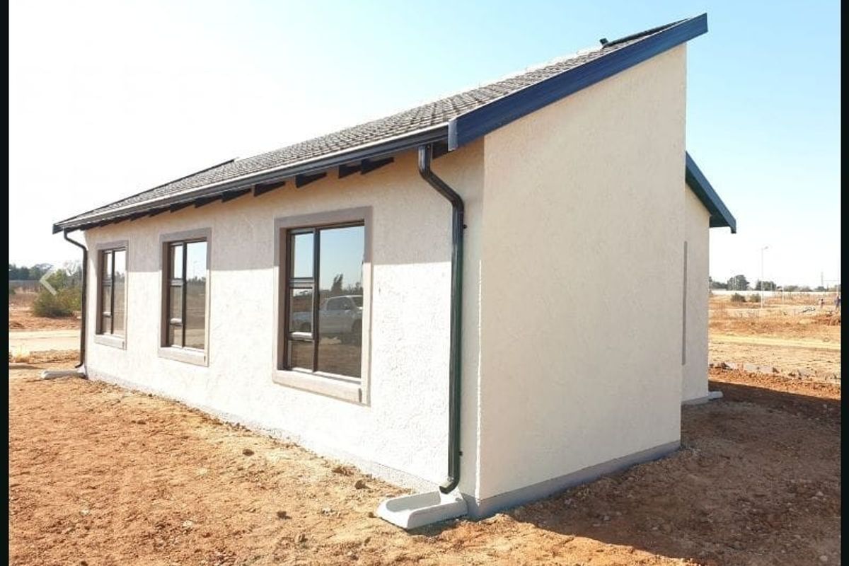 Side and rear view of a modern house featuring a mono-pitch tiled roof, textured exterior walls, and dark aluminium window frames.