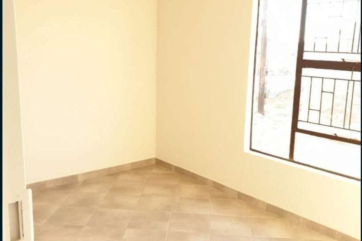 A bright, empty bedroom featuring neutral tiled flooring, a window with security bars, and a fitted curtain rail.
