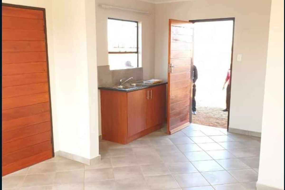 A compact, empty kitchen area featuring tiled flooring, wooden doors, and basic cabinetry with a stainless steel sink.