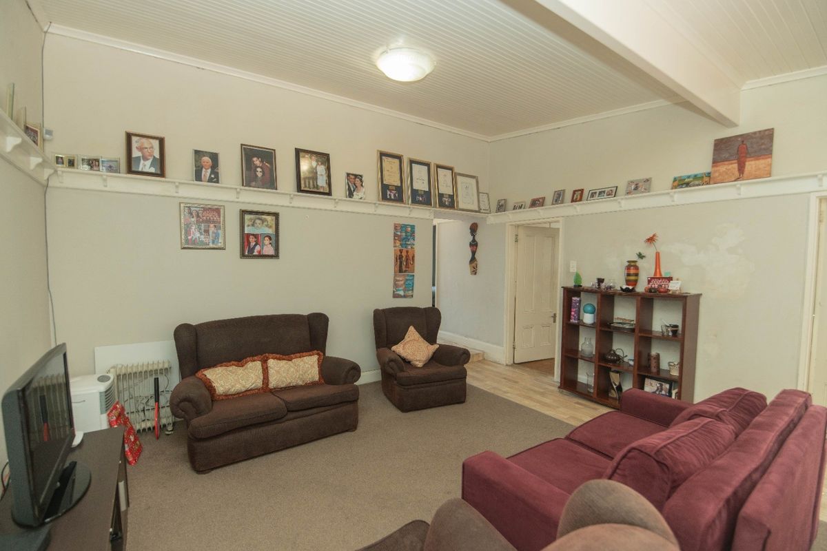 A living room featuring a beadboard ceiling, picture rail, and neutral wall finishes, requiring cosmetic updates to address visible wall surface wear.