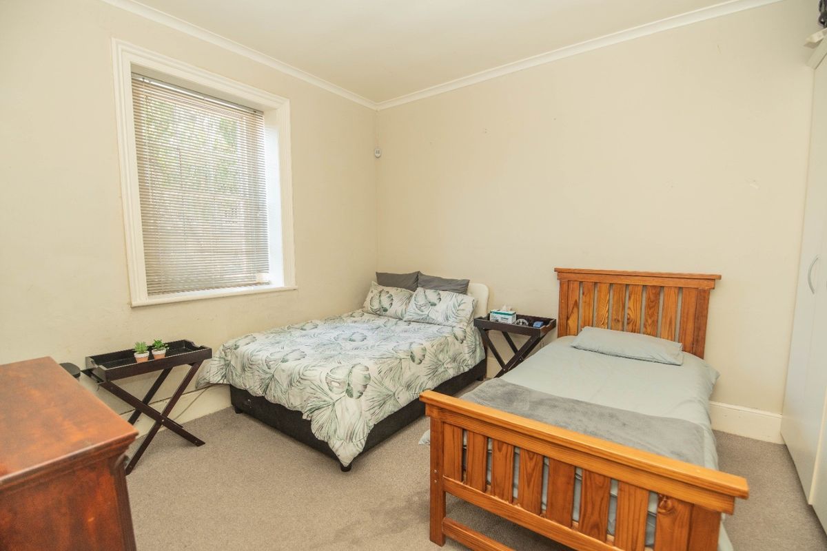 A functional bedroom featuring neutral wall tones, carpeted flooring, a built-in wardrobe, and a window with fitted blinds.