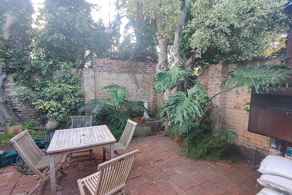 A private rear courtyard featuring a brick-paved patio, established garden surroundings, and a built-in braai area, offering a secluded outdoor entertainment space.