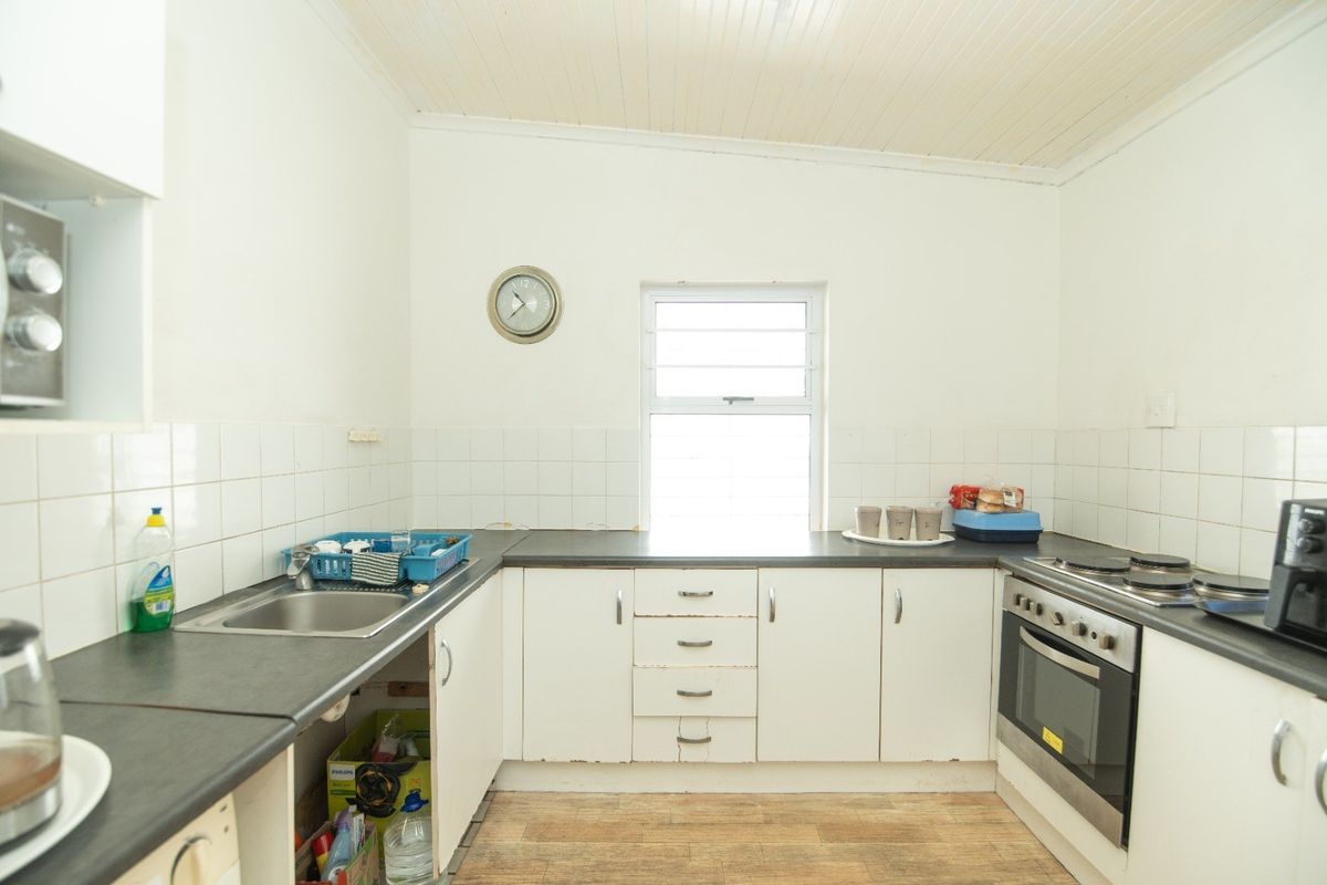 A functional kitchen featuring white cabinetry, dark laminate countertops, a built-in oven, and a tiled splashback, offering potential for cosmetic updates.