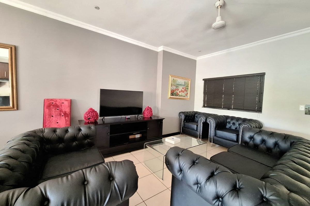 A well-maintained living room featuring neutral grey walls, tiled flooring, recessed downlights, and a ceiling fan, providing a comfortable and functional space.
