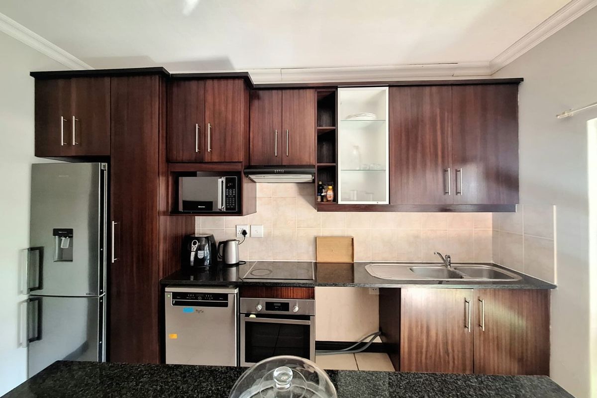 A functional kitchen featuring dark wood cabinetry, granite countertops, built-in oven, hob, and extractor fan with a tiled backsplash.