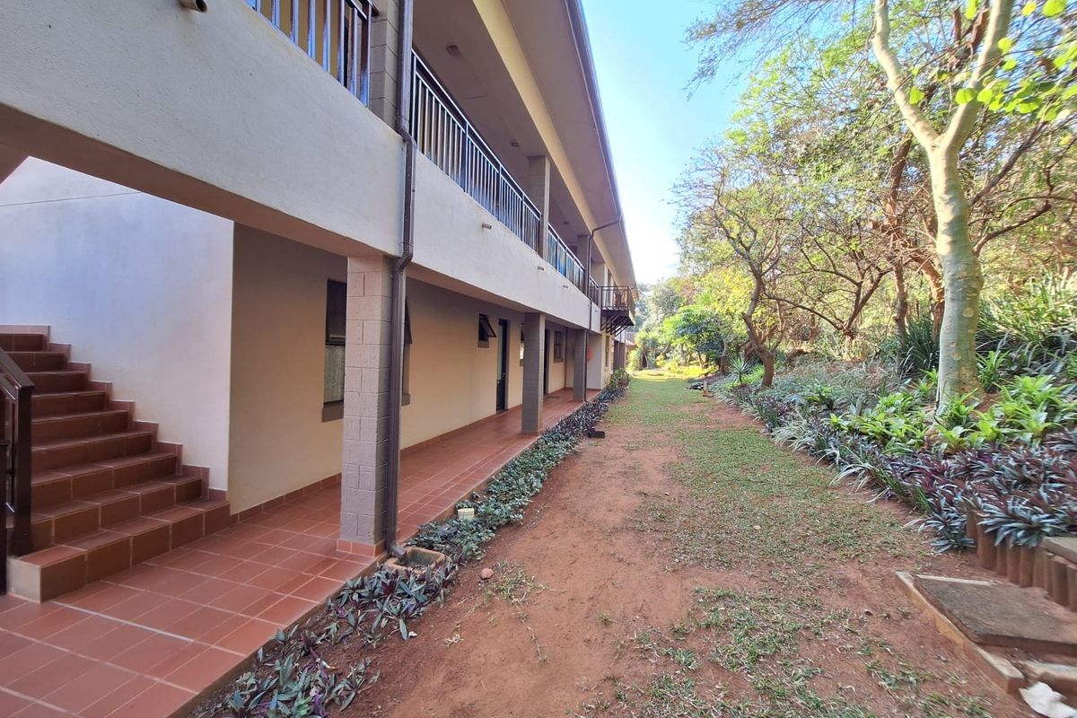 Rear view of the apartment building featuring a covered tiled walkway, metal balustrades, and access to an external staircase overlooking the garden area.