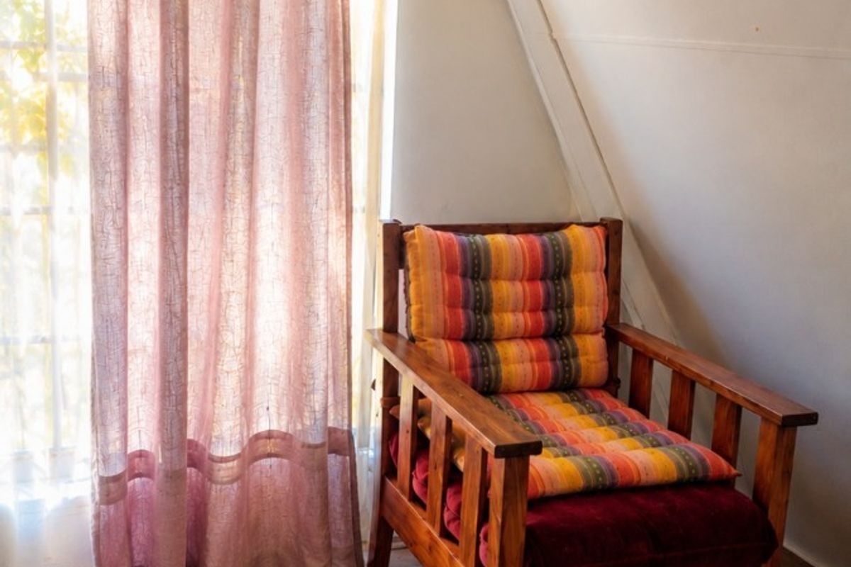A cozy bedroom corner featuring laminate flooring and a distinctive sloped ceiling, illuminated by natural light through a large window.