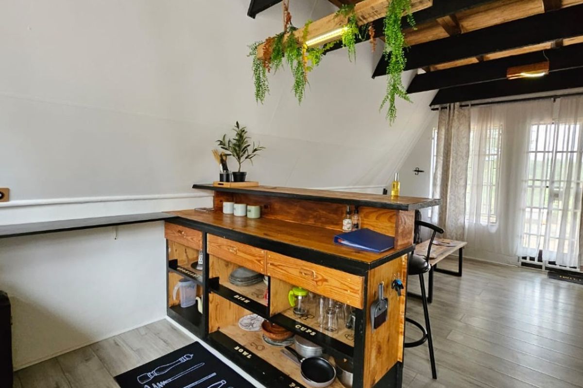 A rustic kitchen area featuring exposed timber ceiling beams, a custom timber island unit, and laminate flooring with access to an outdoor area.