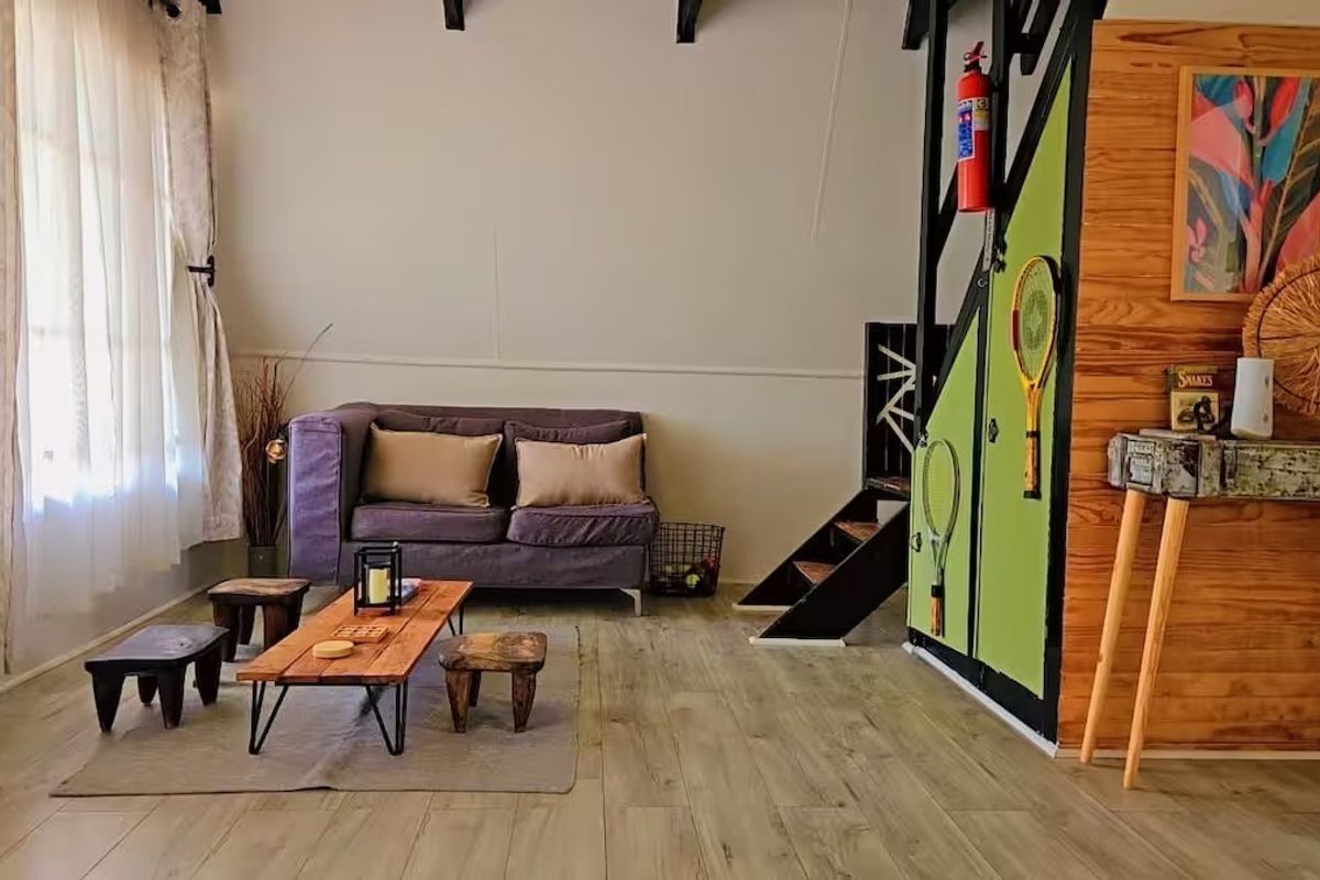 A cozy living room featuring laminate flooring, exposed ceiling beams, and a staircase leading to an upper level.