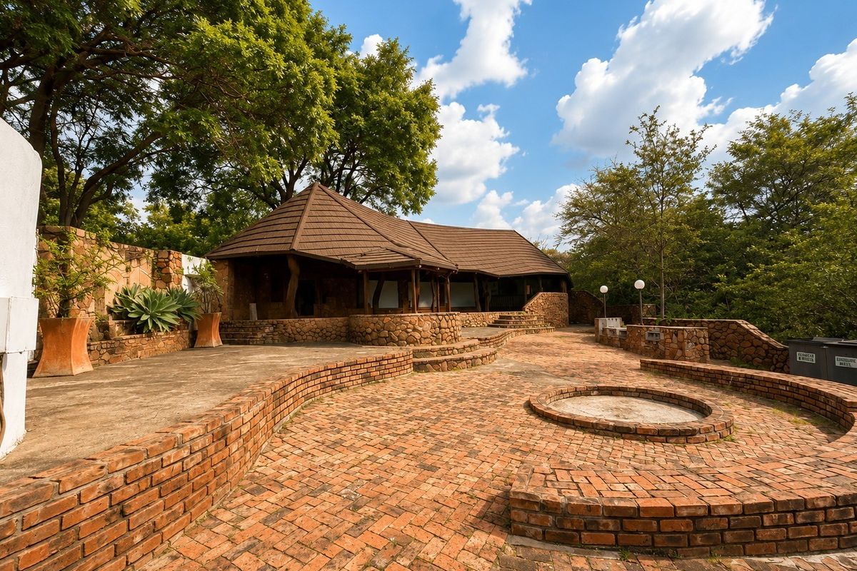 Spacious rear outdoor entertainment area featuring extensive brick paving, stone retaining walls, a built-in fire pit, and a covered patio structure.