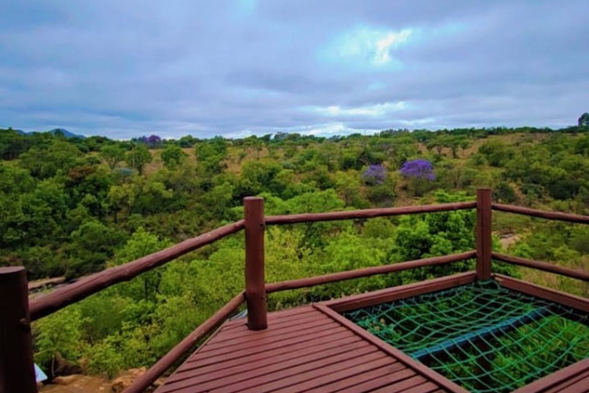 An elevated timber deck balcony featuring a built-in hammock net and panoramic views of the surrounding natural landscape.