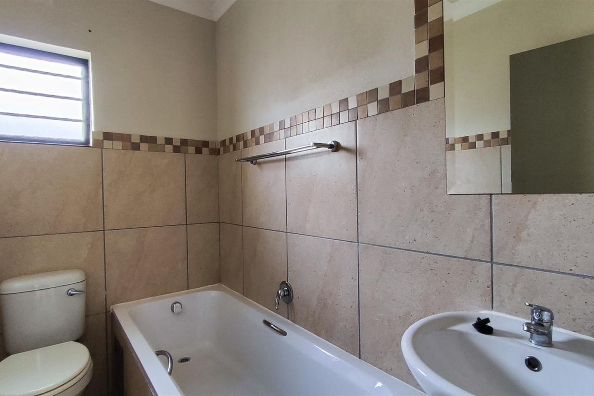 A functional bathroom featuring a bathtub, pedestal basin, and toilet with neutral wall tiling and a wall-mounted mirror.