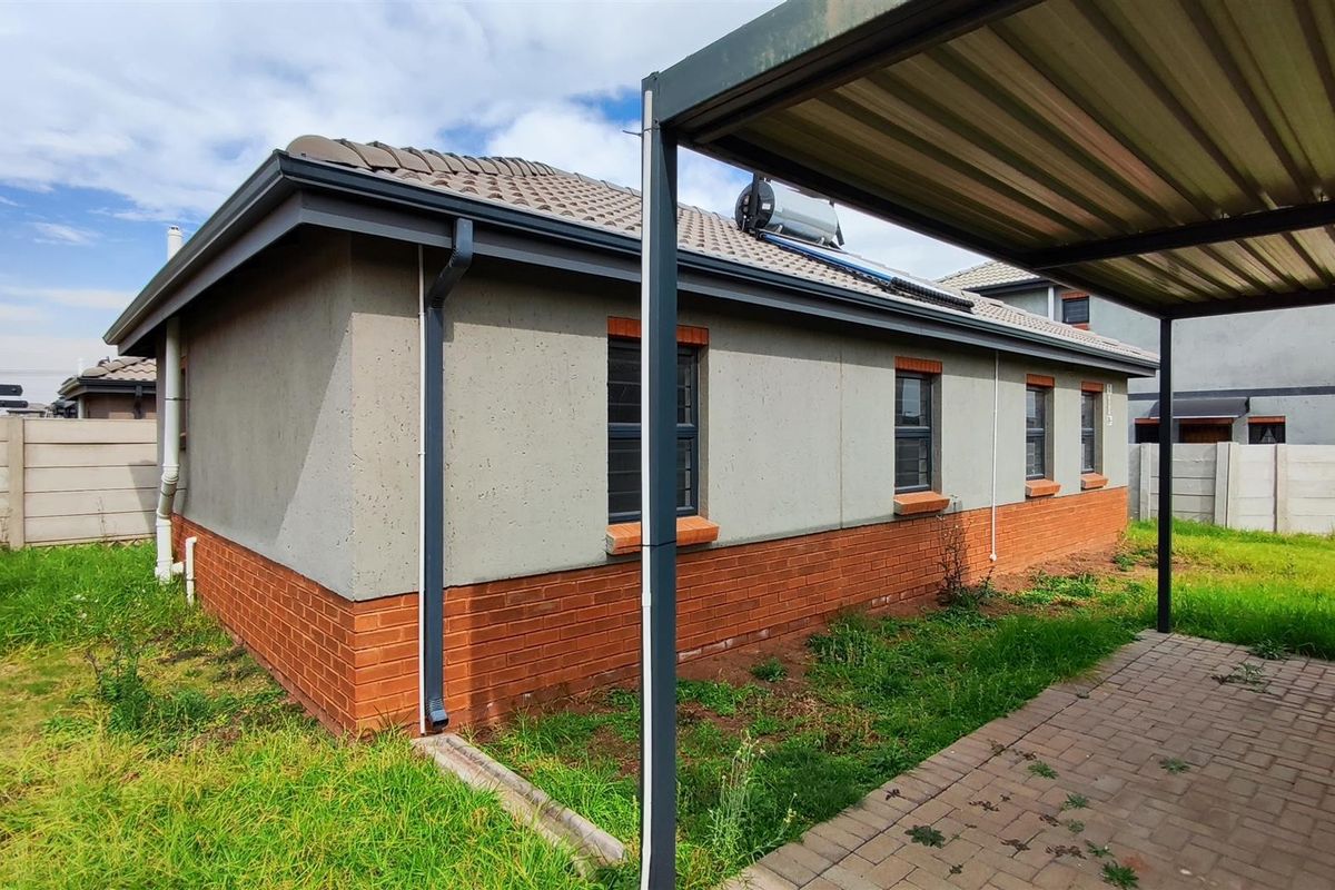 Rear exterior view of the house featuring a brick and plaster facade, tiled roof with solar geyser, and a paved carport area.