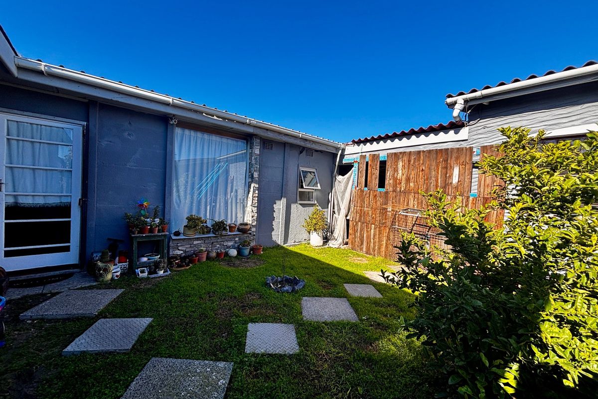 A rear courtyard area featuring a small lawn, paved stepping stones, and timber boundary fencing.