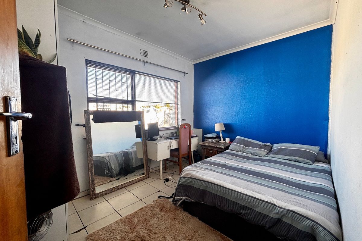 A functional bedroom featuring tiled flooring, a bold blue accent wall, and natural light through aluminium-framed windows.