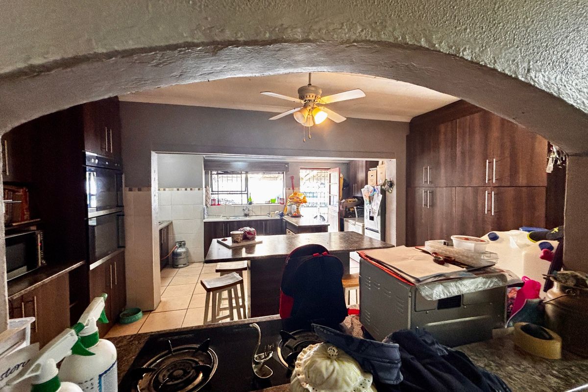 Spacious kitchen featuring dark wood cabinetry, a central island, built-in oven, and tiled flooring, viewed through a decorative arched entryway.