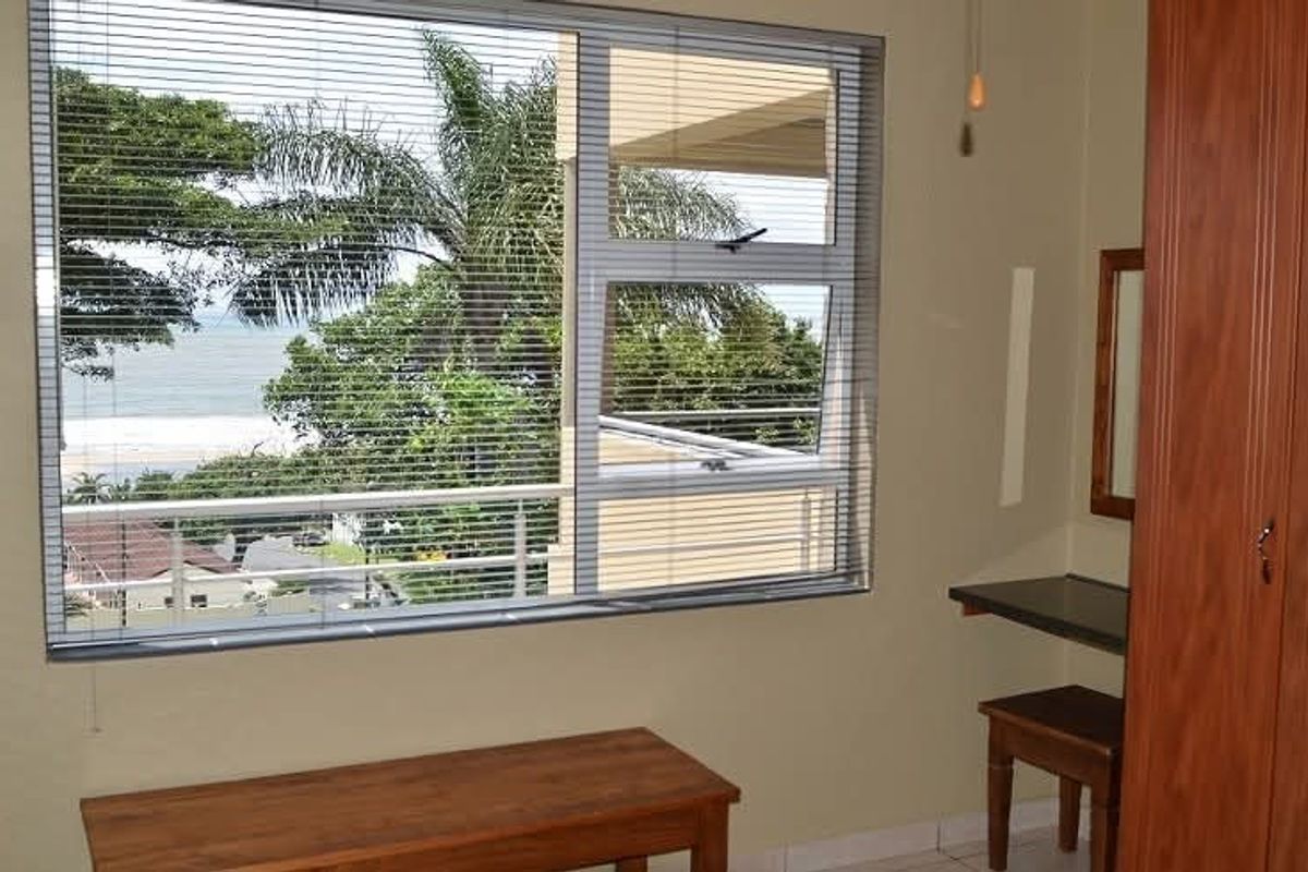 Bedroom featuring a built-in wardrobe, vanity, and large windows with venetian blinds offering scenic coastal views.