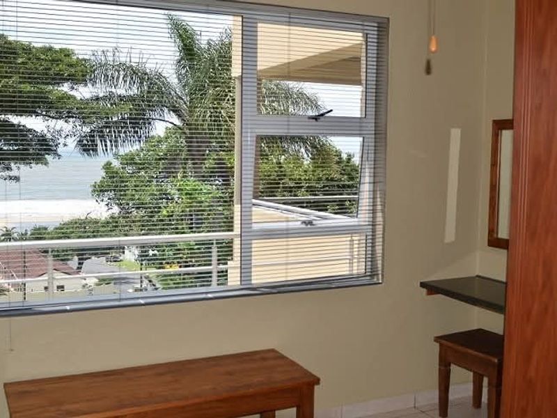 Bedroom featuring a built-in wardrobe, vanity, and large windows with venetian blinds offering scenic coastal views.