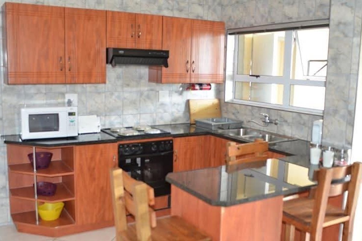 A functional kitchen featuring wood-look laminate cabinetry, granite countertops, a built-in oven with hob, and a double bowl sink with tiled backsplash.