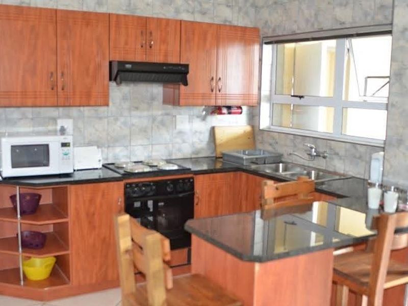 A functional kitchen featuring wood-look laminate cabinetry, granite countertops, a built-in oven with hob, and a double bowl sink with tiled backsplash.