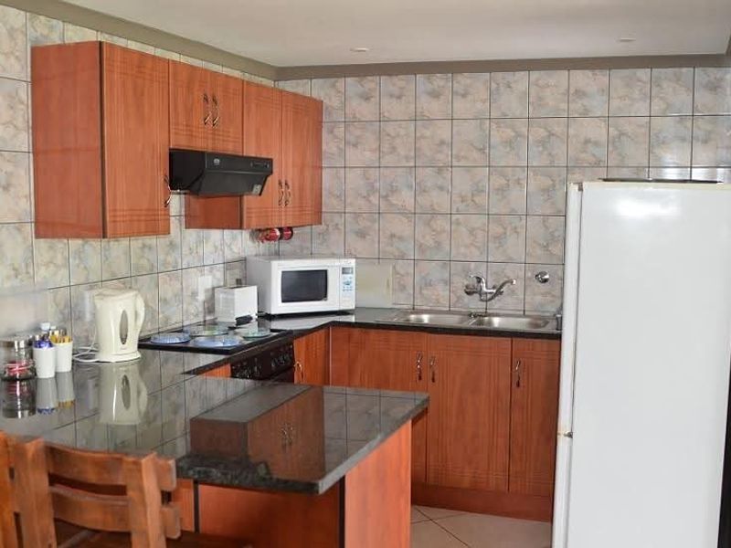 A functional kitchen featuring wood-look laminate cabinetry, granite countertops, a double basin sink, and extensive ceramic wall tiling.
