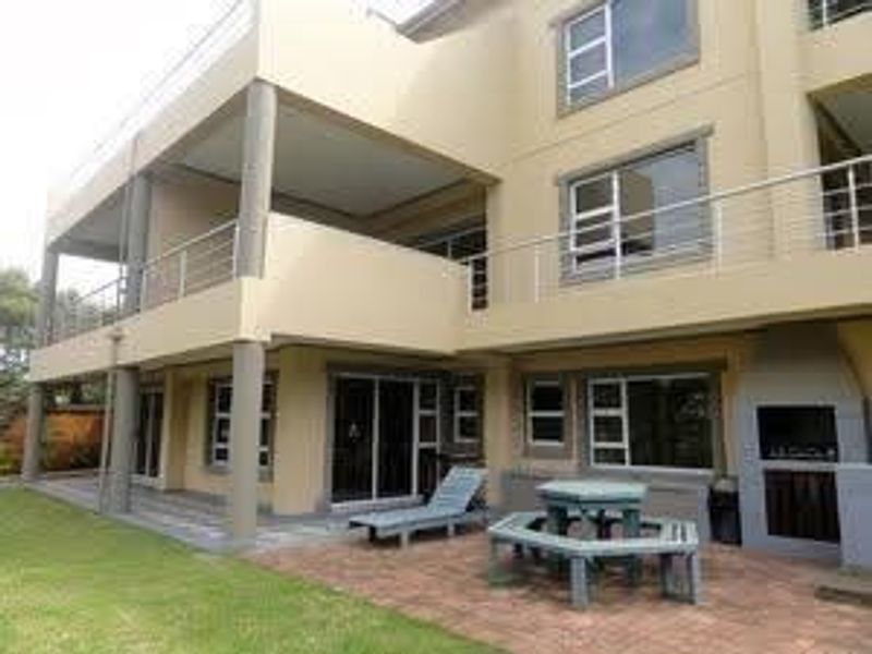 Rear view of a multi-story house featuring a covered patio, upper balcony with stainless steel balustrades, and a built-in outdoor braai area.