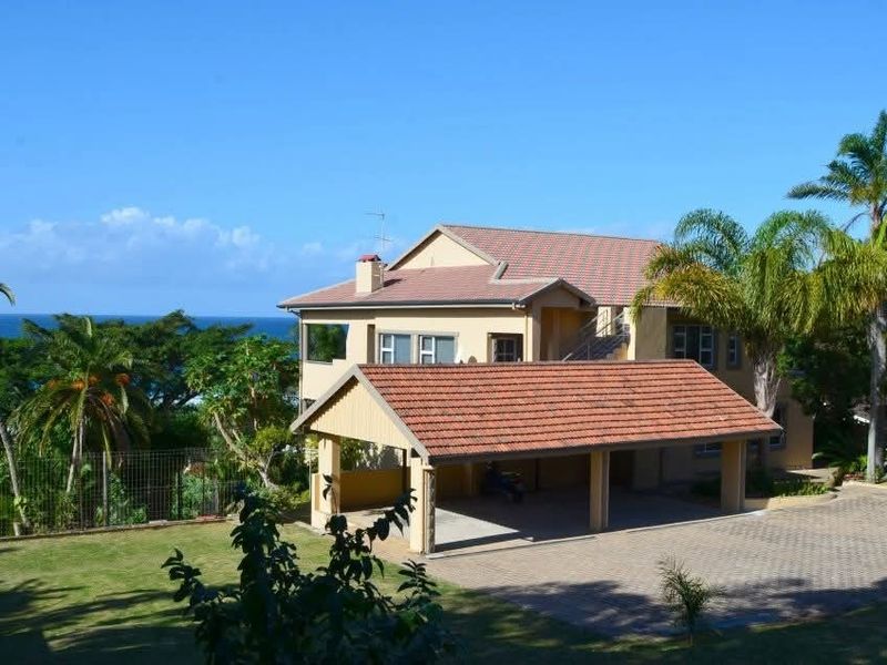 A multi-level residential property featuring a tiled roof, attached carport, and paved driveway, set within a landscaped garden with ocean views.