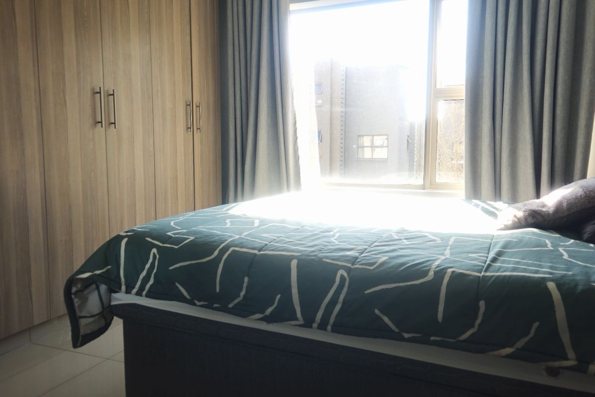 A well-lit bedroom featuring floor-to-ceiling built-in cupboards and tiled flooring, offering a clean and functional living space.