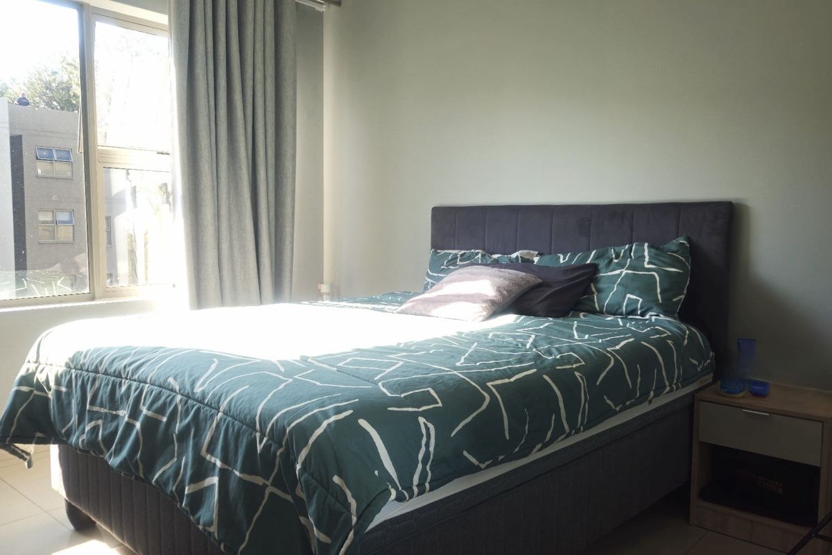 A well-lit bedroom featuring tiled flooring and a large window with curtain tracks, providing a bright and functional living space.