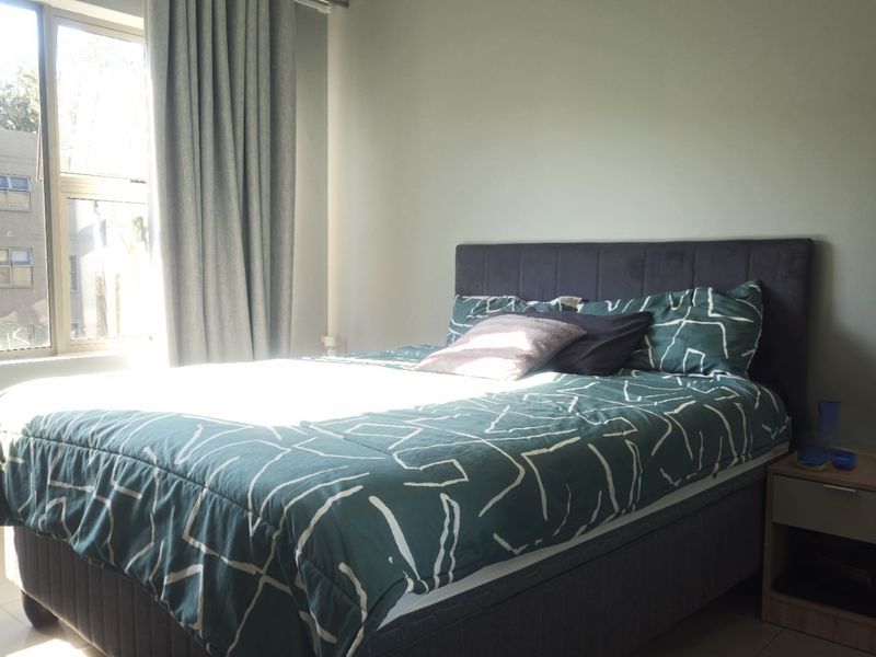 A well-lit bedroom featuring tiled flooring and a large window with curtain tracks, providing a bright and functional living space.