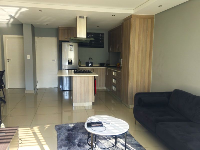 Open-plan living area featuring a modern kitchen with wood-finish cabinetry, a central island with a gas hob, and neutral tiled flooring throughout.