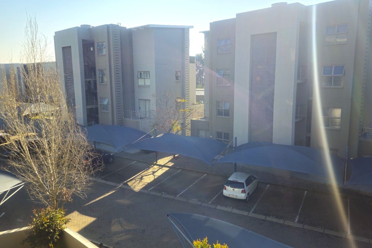 View of the apartment complex exterior featuring paved parking bays with shade-cloth carports and multi-story residential building facades.